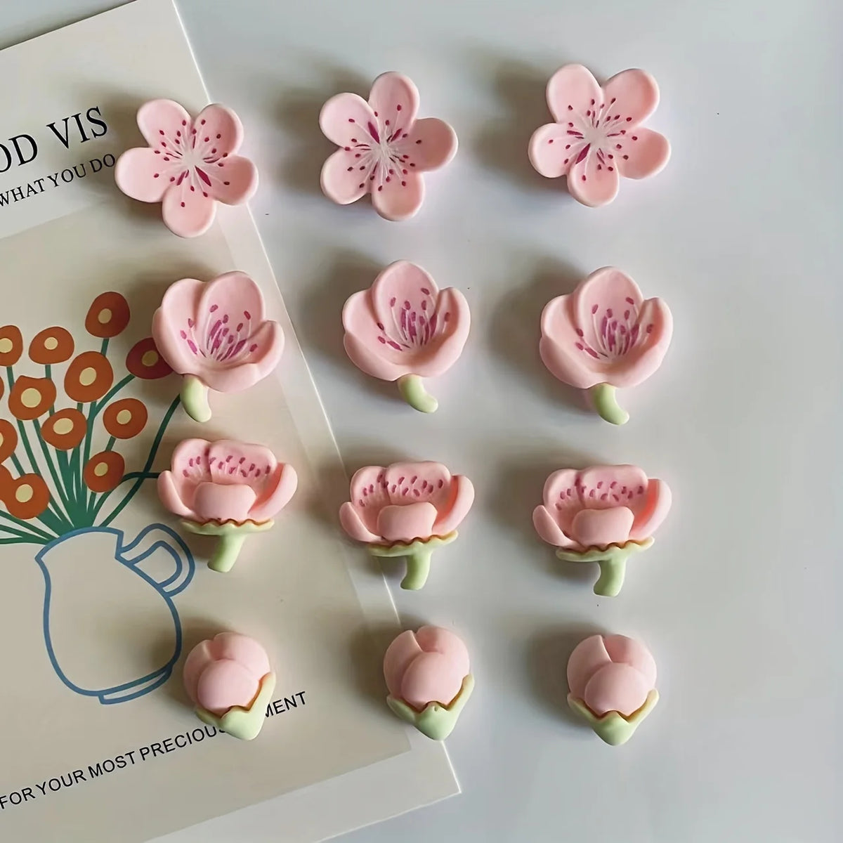 A set of twelve pink and white flower decorative fridge magnets with green stems displayed on a light background.