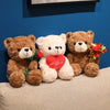 Three teddy bears, one brown, one white, and one brown, with a red heart on the chest, set against a blue wall.