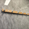 A wooden coat rack with eight hooks and a storage shelf mounted on a gray stone wall.