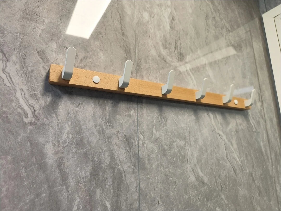 A wooden coat rack with eight hooks and a storage shelf mounted on a gray stone wall.