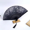 Black folding fan with white floral patterns mounted on a wooden base