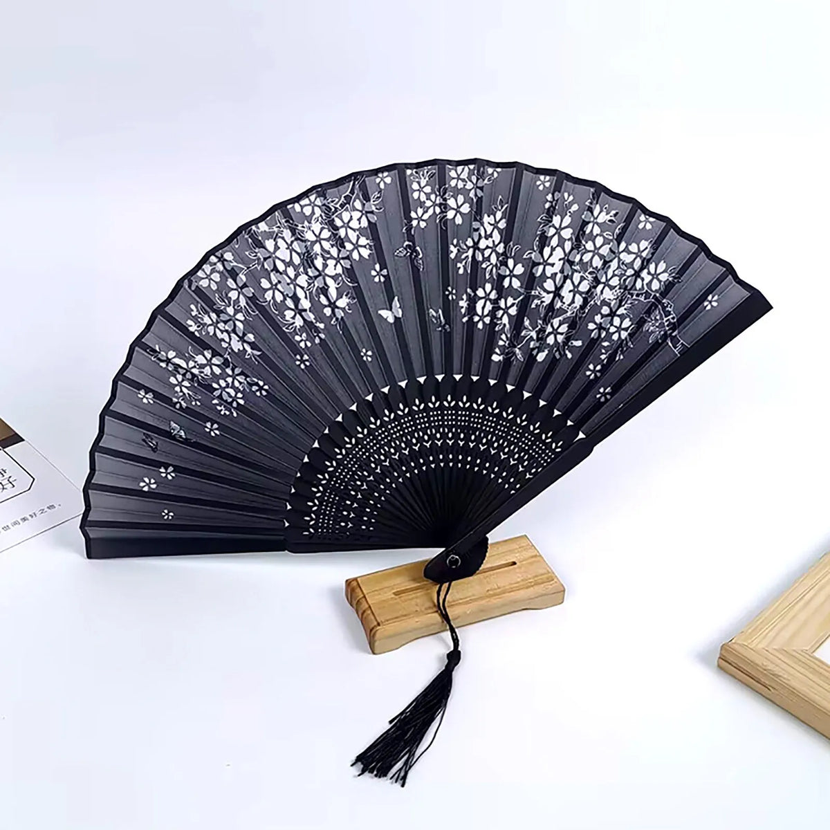 Black folding fan with white floral patterns mounted on a wooden base