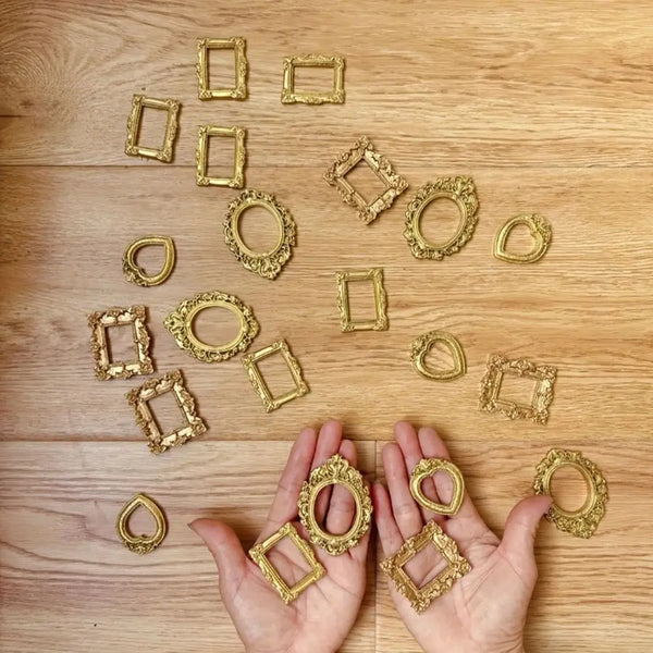 A hand holds several vintage gold resin shadow box frames on a wooden surface.