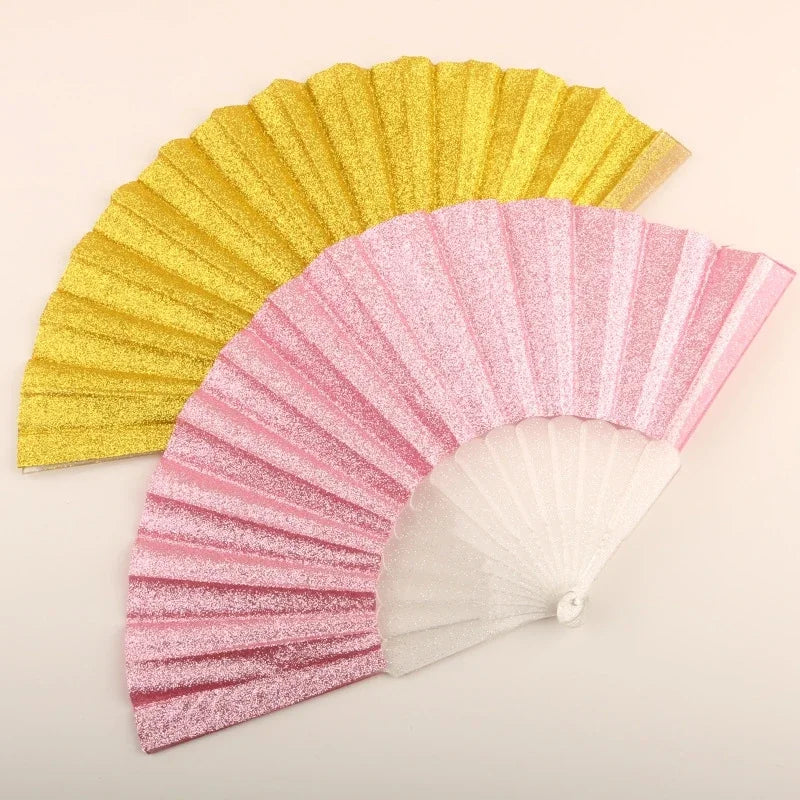 A folding fan made of glitter material, featuring a gradient color transition from yellow to pink.