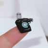 A black vintage rotary desk phone miniature decor resting on a finger against a white background.