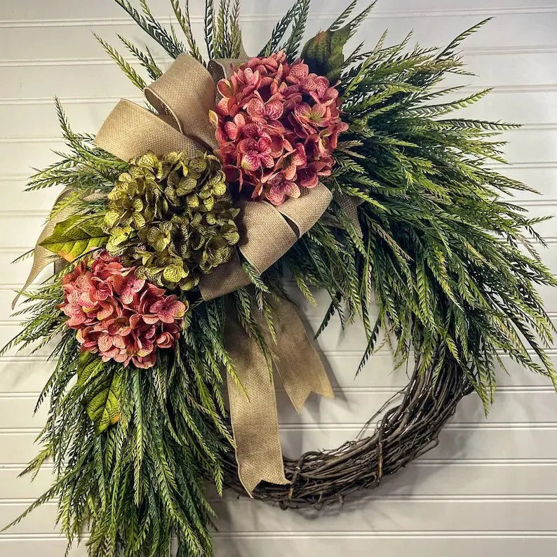 A rustic wreath made of green foliage and pink hydrangea flowers tied with a natural burlap bow.