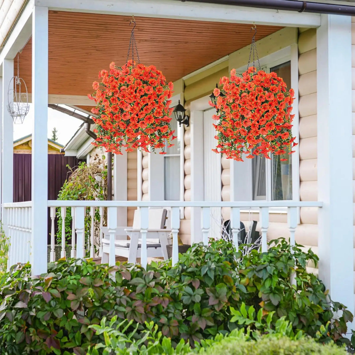 Two hanging planters filled with bright orange artificial morning glory flowers and eucalyptus decor on a porch.