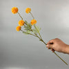 Una mano sostiene un tallo con varias flores artificiales de margarita de chrysanthemum amarillo brillante y hojas verdes con
