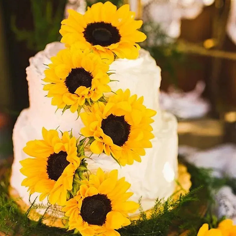 A white cake decorated with bright yellow artificial sunflower heads.