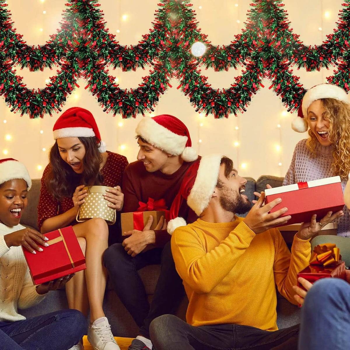 A group of people laughing while decorating a Christmas tree with a festive tinsel garland.