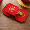 Two red felt charms with gold emblems are displayed on a wooden surface next to a gold-colored hat.