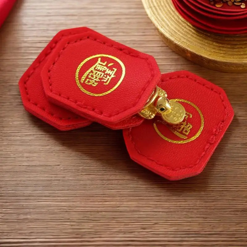 Two red felt charms with gold emblems are displayed on a wooden surface next to a gold-colored hat.