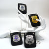Una mano sostiene varios collares de credenciales policiales realistas con emblemas de plata y oro en tela negra.