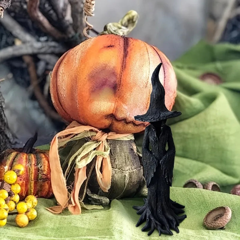 Una estatua de bruja oscura de material negro se sienta sobre una calabaza y decoración rústica de madera.