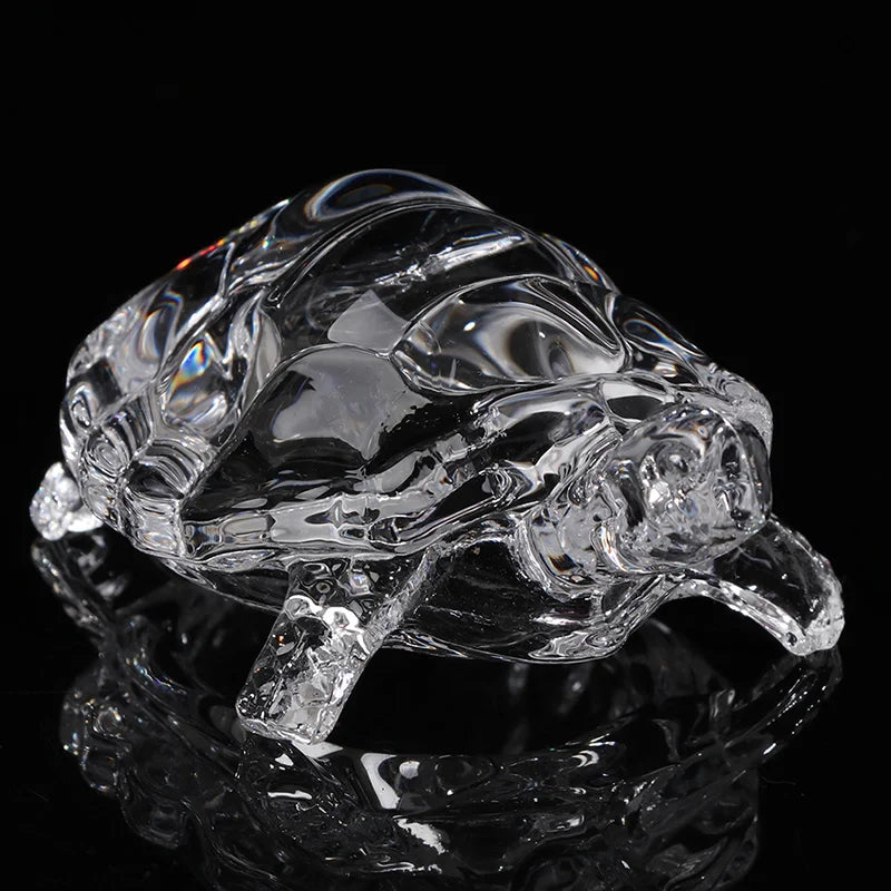 A clear glass miniature tortoise statue reflecting on a dark surface.