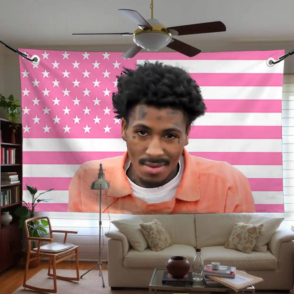 A young man with dreadlocks wearing an orange shirt is centered against a pink and white striped flag banner.
