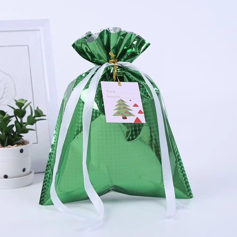 A green festive drawstring gift bag with a gold tag featuring a Christmas tree and snowman design.