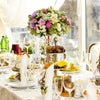 A crystal flower centerpiece stand with candles decorated with various fresh flowers on a white tablecloth.