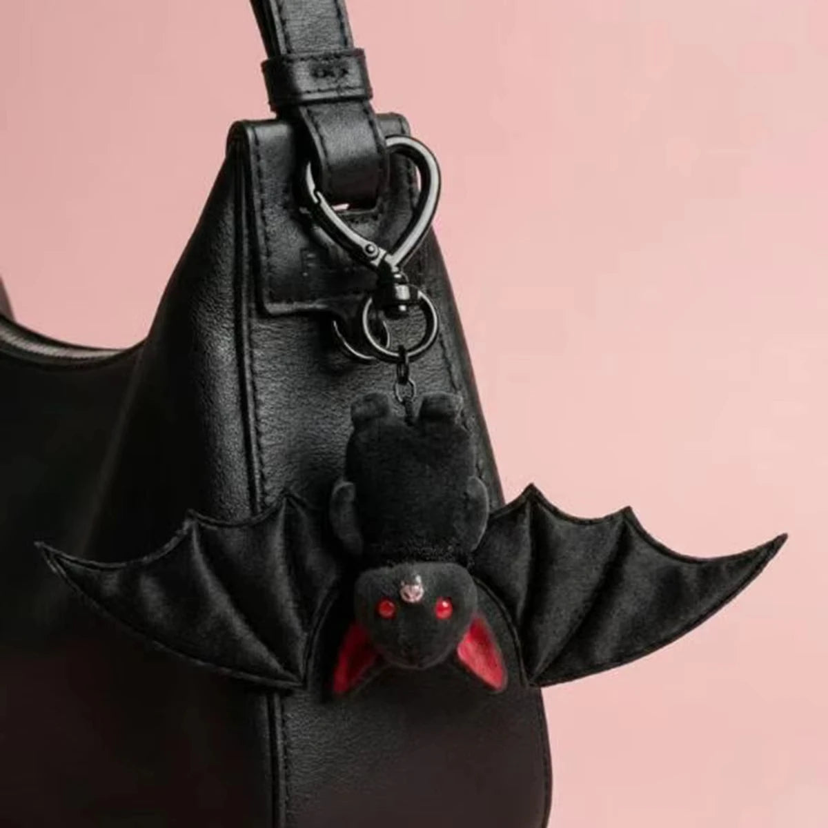 A black faux leather handbag with a bat-themed charm attached to the strap.