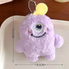 A purple fuzzy plush monster with a yellow ear and a large eye is displayed on a white tray.