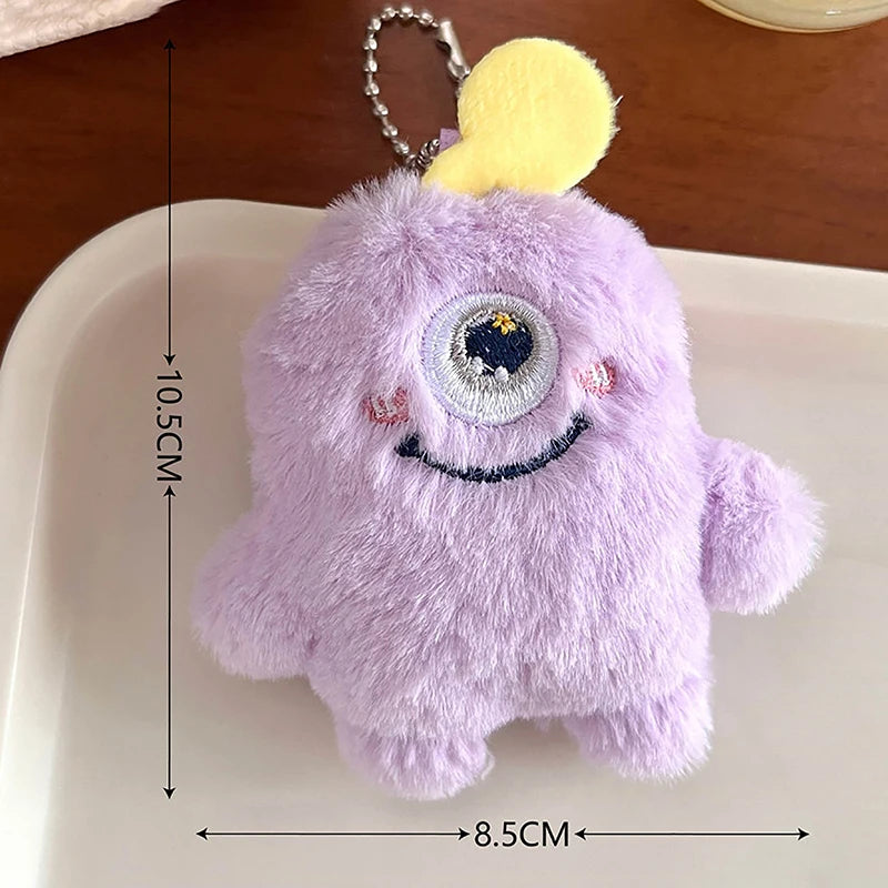 A purple fuzzy plush monster with a yellow ear and a large eye is displayed on a white tray.