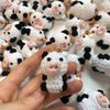 A hand holds a handmade crochet cow keychain featuring white and black wool with pink accents.