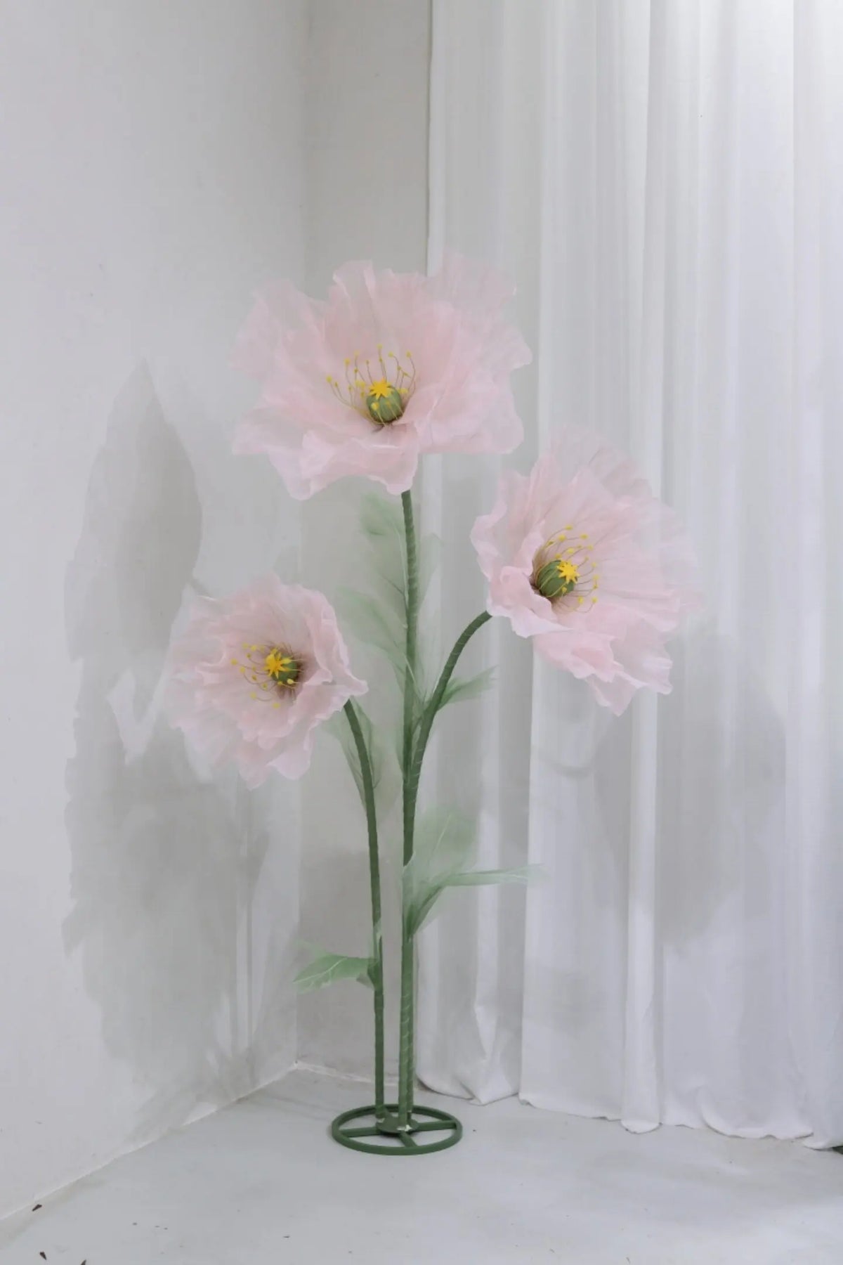 A large artificial silk pink poppy flower displayed on a green stand against a white background.