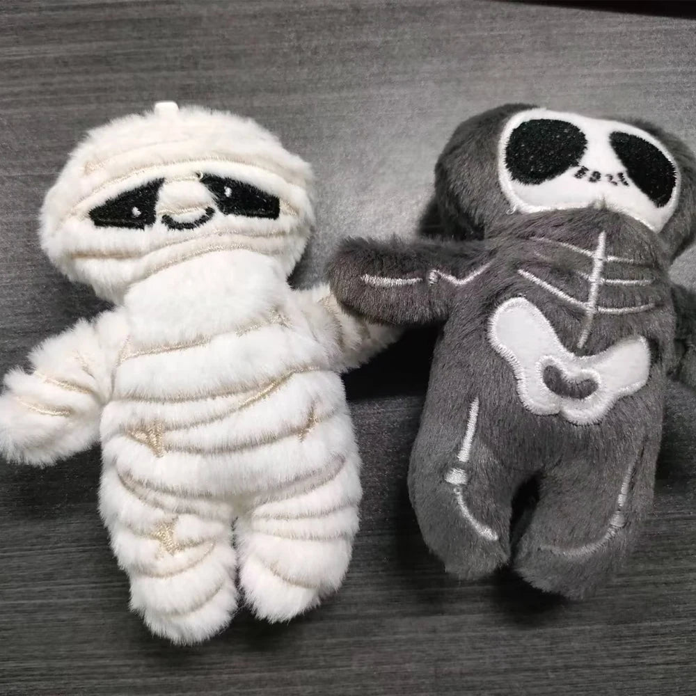 A white mummy skeleton plush toy next to a gray mummy skeleton plush toy.