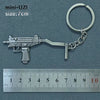 A silver miniature assault rifle model keychain with a metal ring attached, shown next to a ruler.