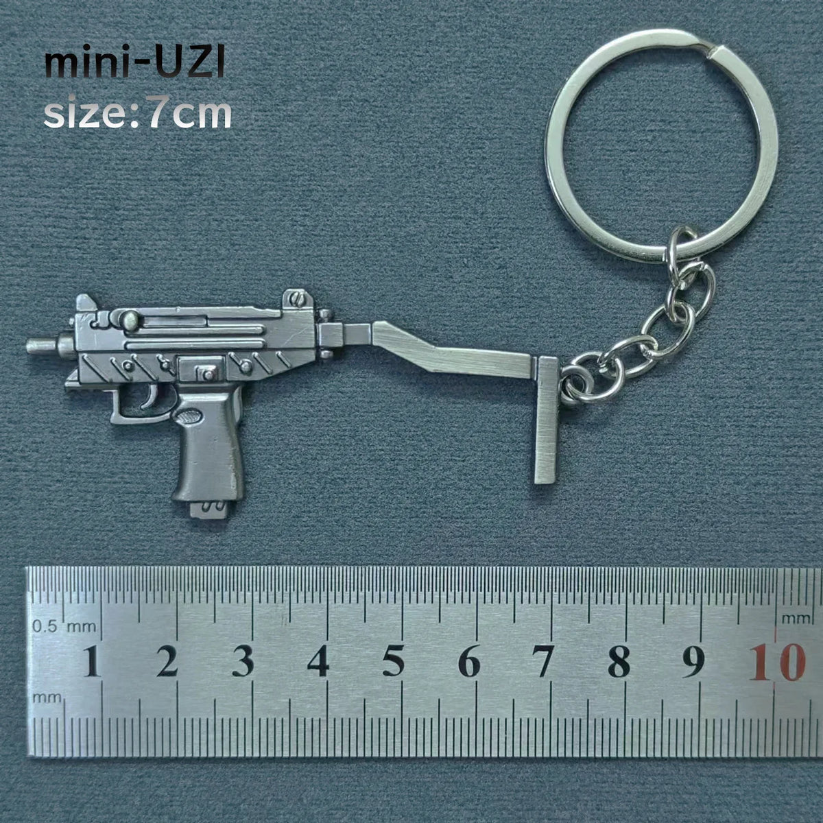 A silver miniature assault rifle model keychain with a metal ring attached, shown next to a ruler.