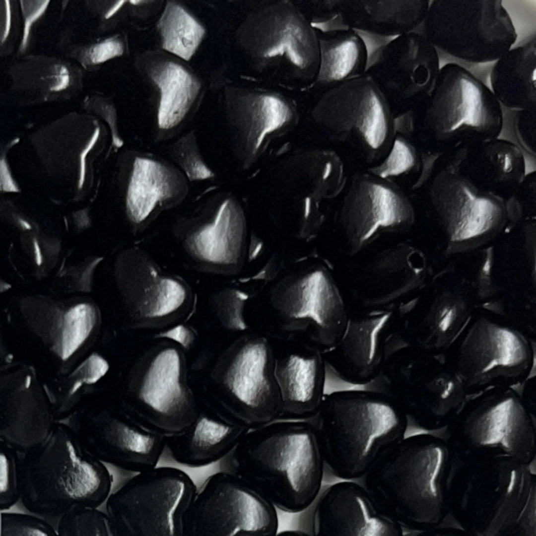 A close-up view of small, glossy black heart-shaped acrylic decoration beads.