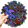 Une main tient un autocollant de dinosaure violet lumineux sur un fond de stickers style graffiti colorés.