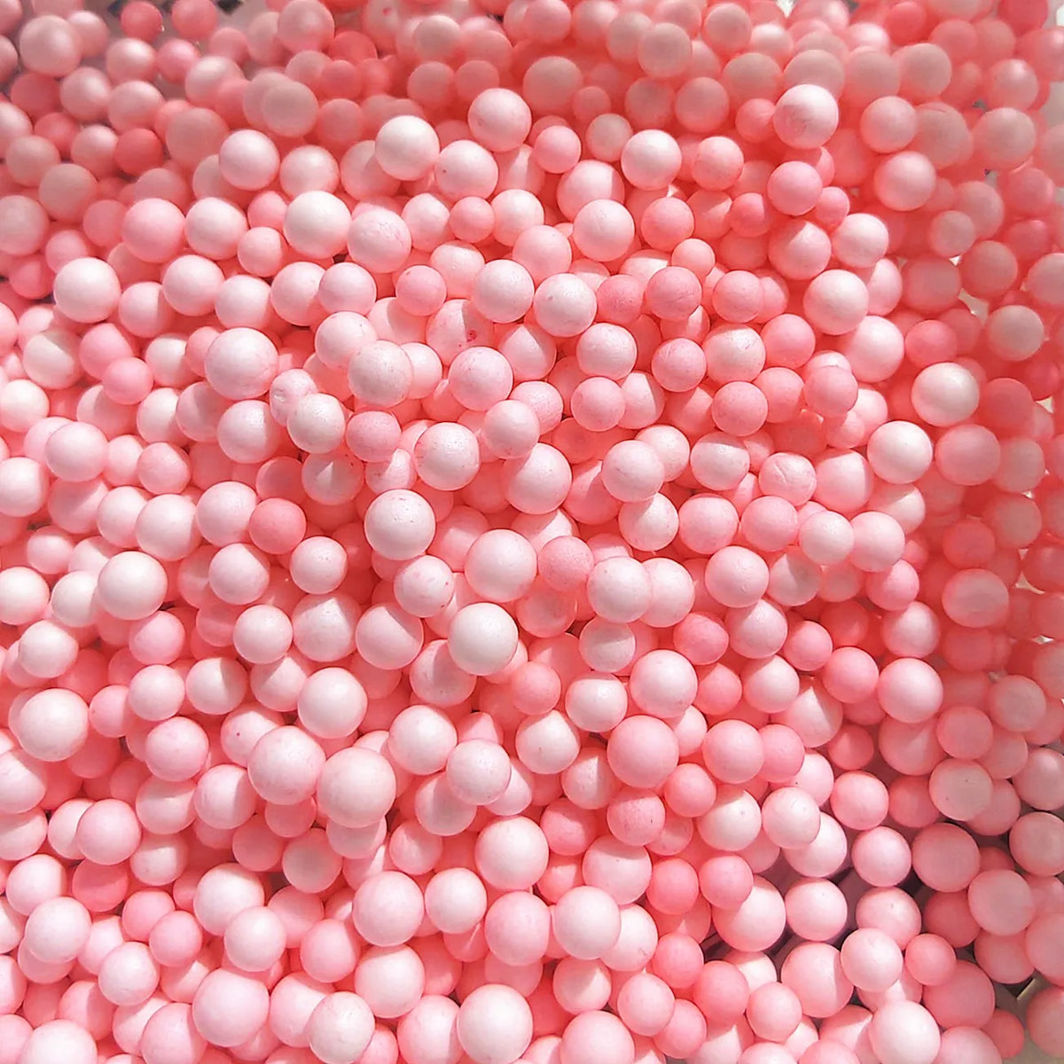 A close-up view of numerous small, round pink foam beads for crafting and decoration.