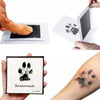 A handprint and footprint ink pad kit showing a paw print design on paper and tattooed on skin.