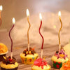 A set of curved decorative birthday candles placed among cupcakes on a wooden surface.