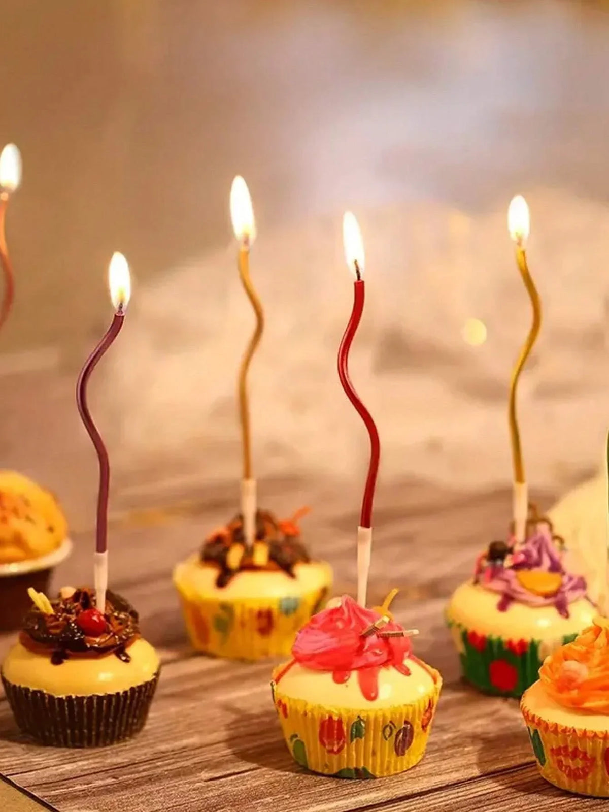 A set of curved decorative birthday candles placed among cupcakes on a wooden surface.