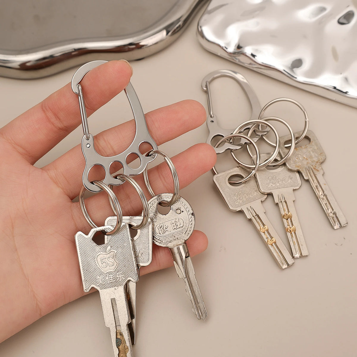 A hand holds a set of durable stainless steel keychains with multi-loop designs and various key shapes.