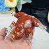A hand holds a resin craft decoration shaped like an orange-brown frog with clear limbs and gold accents.