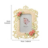 A decorative resin photo frame with a gold border and floral accents, featuring a light pink background.