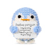 A light blue crocheted penguin plush holding a white card with an encouraging message.