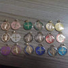 A collection of twelve double-sided St. Benedict medals in various colors and finishes arranged on a surface.