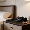 A black draped reclining female statue sculpture rests on a dark wooden nightstand.