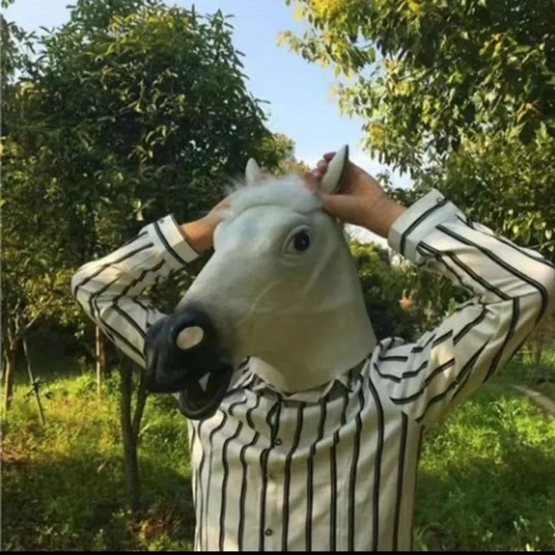 A person is holding a realistic white horse mask with black features outdoors.