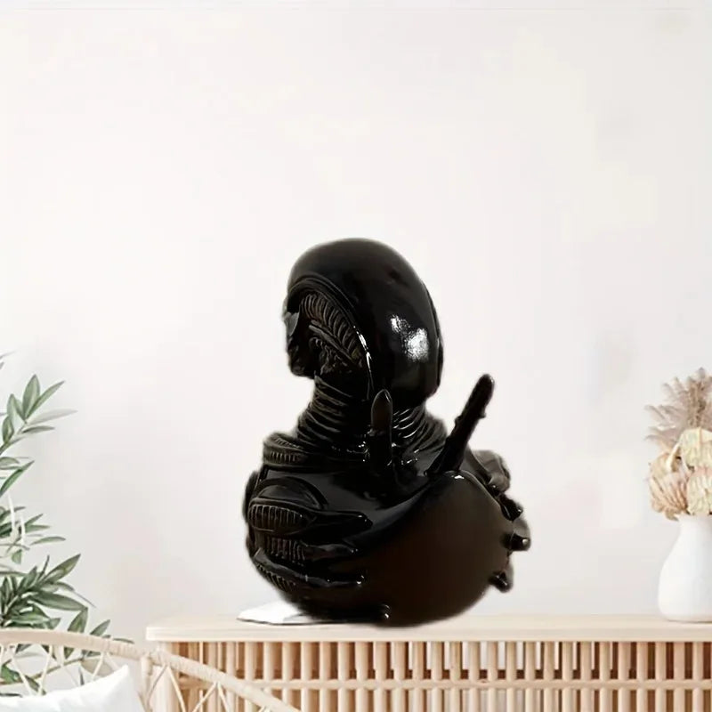 A glossy black resin statue of an alien duck, displayed on a light wooden surface.
