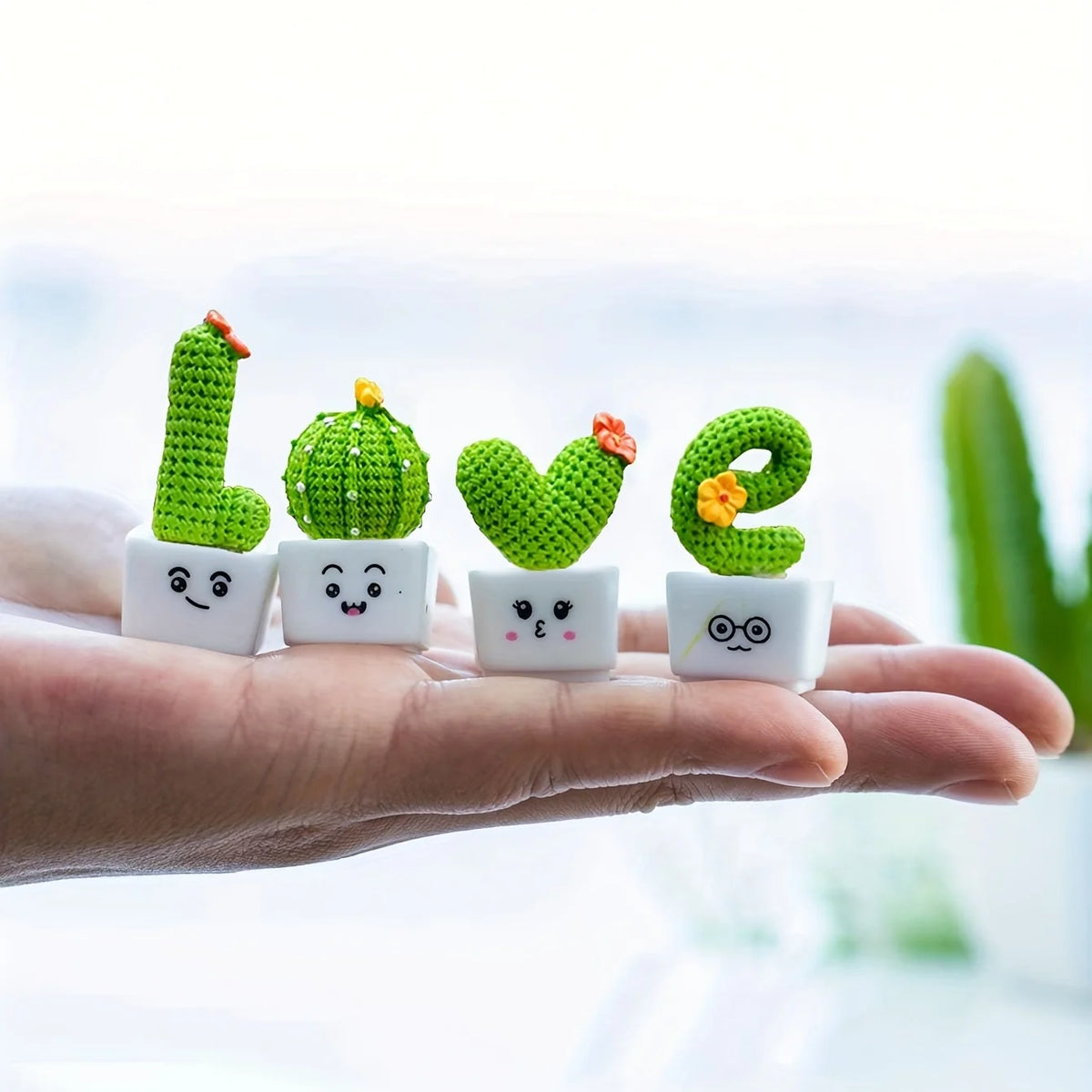 A hand holds a set of four resin succulent cacti shaped like letters L, G, V, and E for home decor.