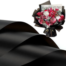 A bouquet of red and white flowers wrapped in black paper with a sign reading Flowers Studio