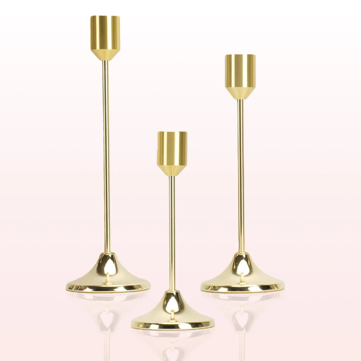 A set of three modern gold metal taper candle holders with slender stems and flared bases.