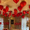 A room decorated with red heart foil balloons and streamers, featuring a 'LOVE' banner backdrop.