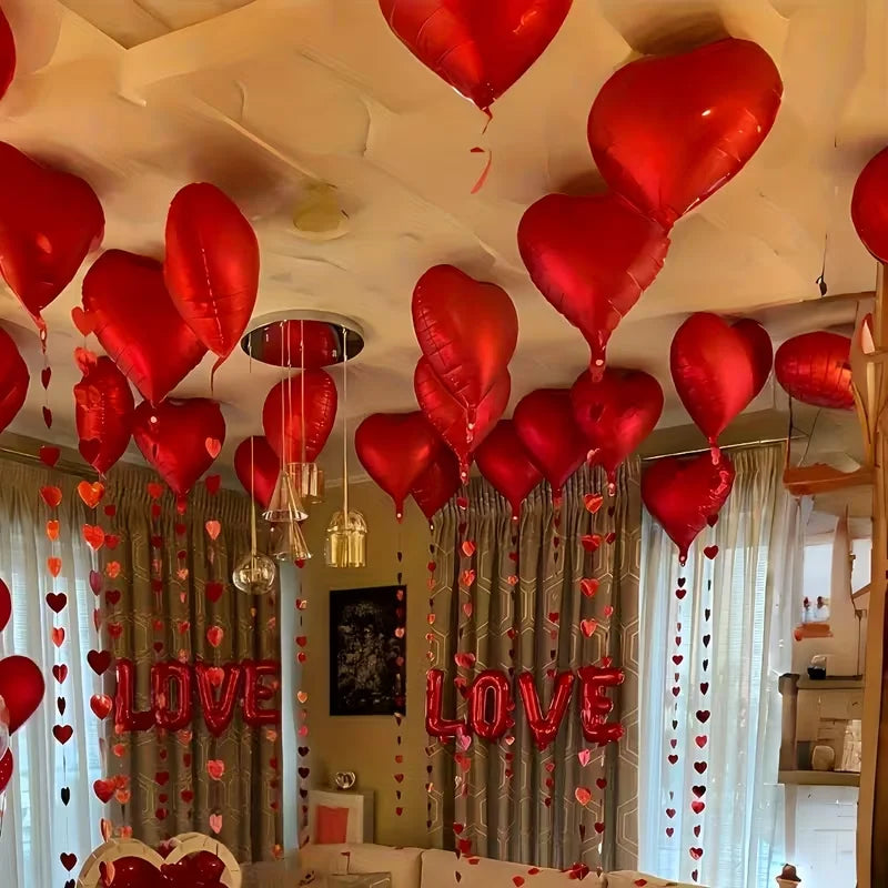 A room decorated with red heart foil balloons and streamers, featuring a 'LOVE' banner backdrop.