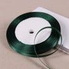 A spool of dark green satin ribbon for gift wrapping and DIY crafts resting on a light surface.